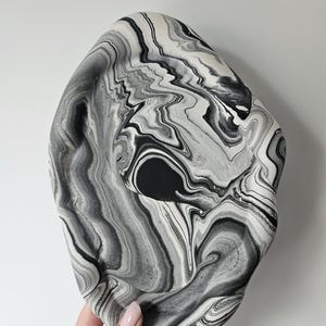 May include: A black and white marbled ceramic bowl with a wavy, organic shape. The bowl is made of a smooth, glossy ceramic and has a unique, abstract design.