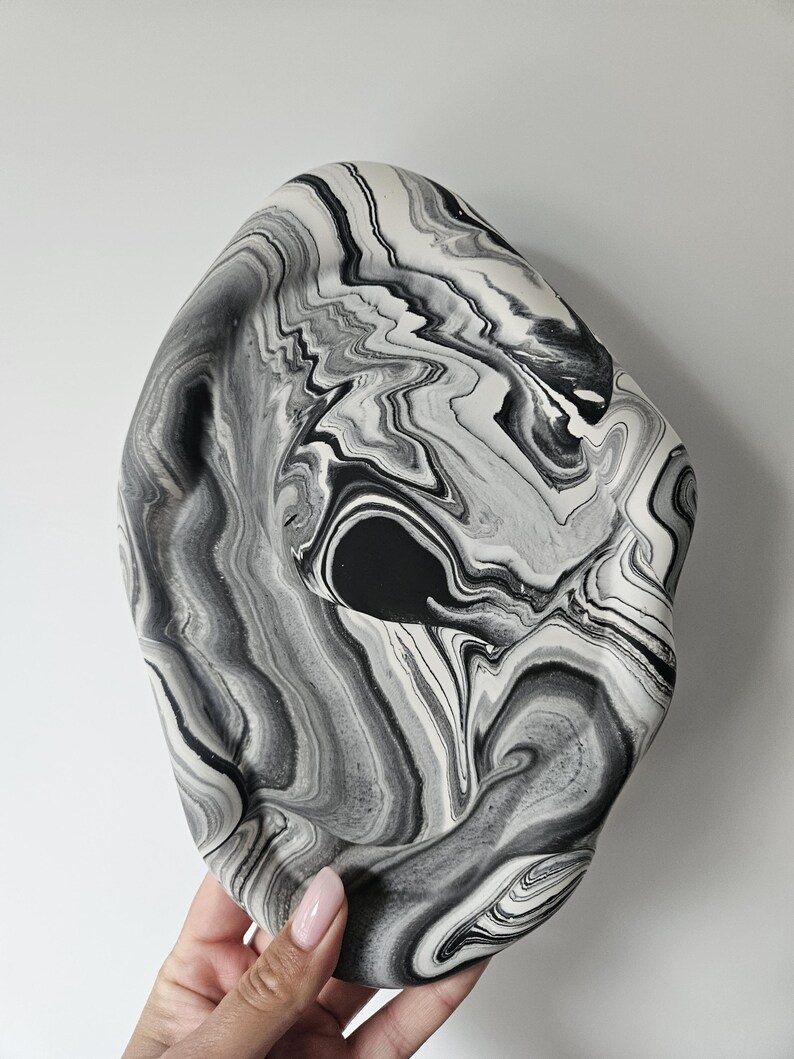 May include: A black and white marbled ceramic bowl with a wavy, organic shape. The bowl is made of a smooth, glossy ceramic and has a unique, abstract design.