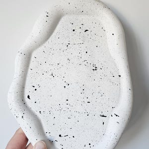 May include: White ceramic tray with a speckled black and white design. The tray has an irregular, organic shape.