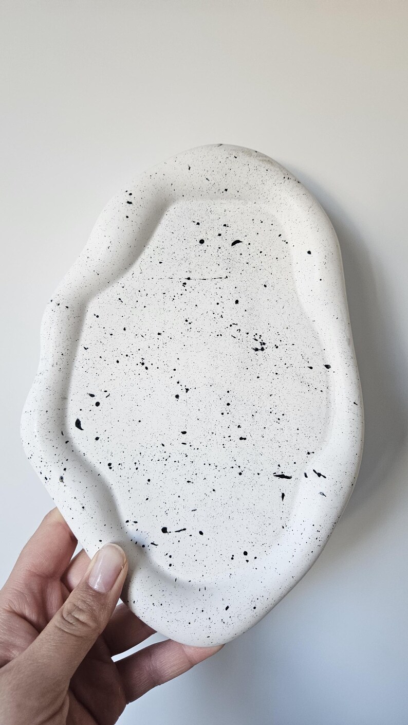 May include: White ceramic tray with a speckled black and white design. The tray has an irregular, organic shape.