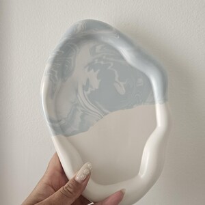 May include: A white ceramic tray with a light blue marbled design. The tray has an irregular shape and a raised edge.