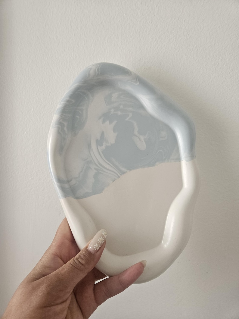 May include: A white ceramic tray with a light blue marbled design. The tray has an irregular shape and a raised edge.