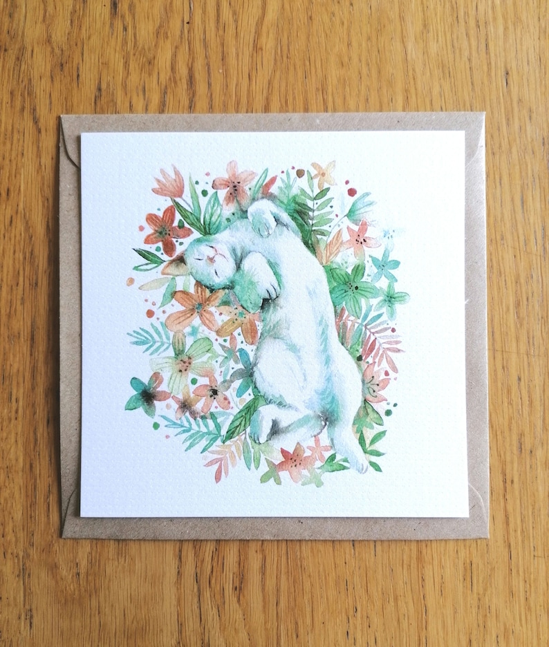 May include: A watercolor painting of a white cat curled up in a circle, sleeping in a bed of green leaves and orange flowers.