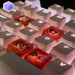 Könnte beinhalten: Nahaufnahme einer weißen Tastatur mit roten und orangen Tastenkappen mit verschiedenen Designs. Die Tastenkappen sind durchsichtig und haben eine glänzende Oberfläche.