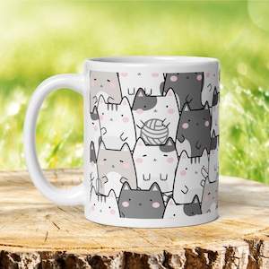 Pode incluir: Caneca de cer&acirc;mica branca com um padr&atilde;o de gatos de desenho animado cinza, branco e preto. Alguns dos gatos est&atilde;o segurando novelos de l&atilde;.