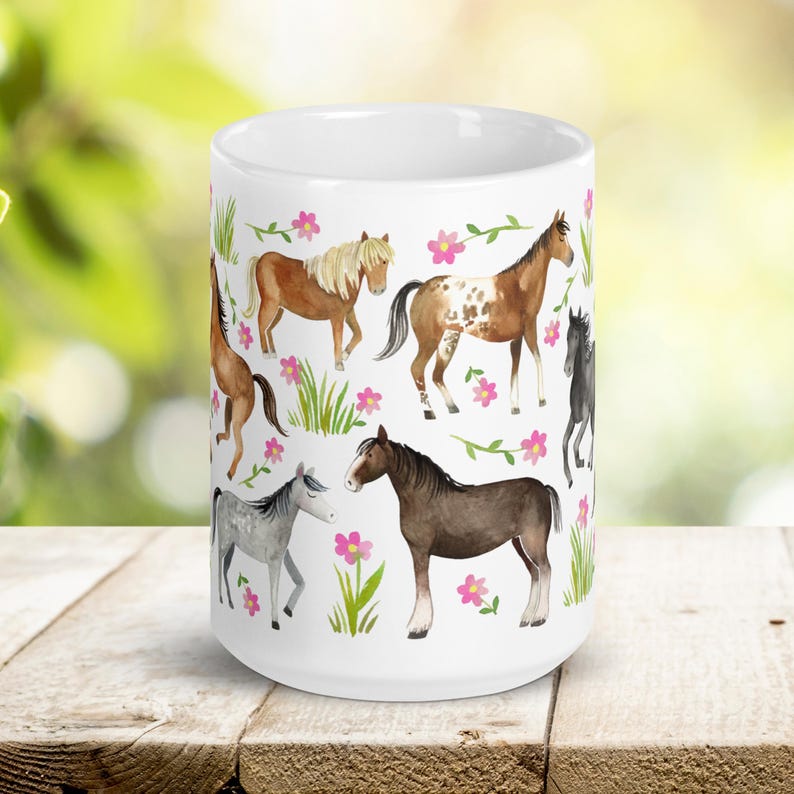 May include: White ceramic mug with a colorful pattern of horses and pink flowers. The horses are brown, black, white, and brown and white.