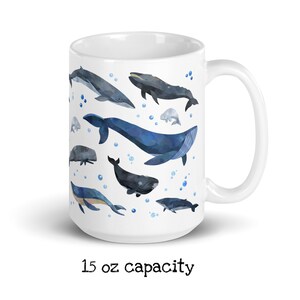May include: White ceramic mug with a watercolor design of various whales in shades of blue and gray. The mug has a 15 oz capacity and is printed with the text "15 oz capacity".