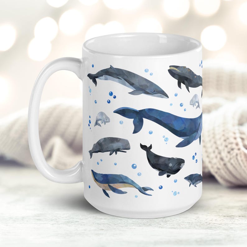 May include: White ceramic mug with a blue and gray watercolor design of various whales and dolphins. The mug has a large handle and is decorated with a repeating pattern of the sea creatures.