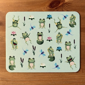 Puede incluir: Un fondo azul claro con un patrón repetido de ranas verdes, libélulas y nenúfares. Las ranas están en varias poses, algunas están sentadas, otras están saltando y otras están nadando. Las libélulas vuelan alrededor de las ranas y los nenúfares. Los nenúfares son verdes y tienen flores blancas.