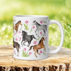May include: White ceramic mug with a colorful watercolor design of horses and flowers. The horses are brown, black, gray, and white. The flowers are pink.