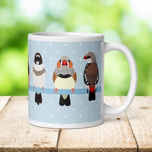 Può includere: Tazza in ceramica bianca con sfondo blu e un motivo a pois bianchi. Quattro diversi tipi di fringuelli sono appollaiati su un ramo, con i becchi rivolti in avanti. I fringuelli sono marroni, bianchi e rossi.