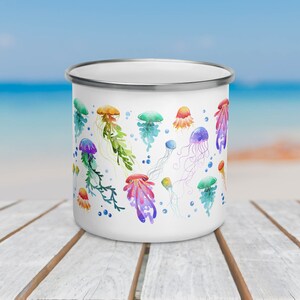 Pu&ograve; includere: Tazza di smalto bianco con un design ad acquerello colorato di meduse. Le meduse sono di varie tonalit&agrave; di rosa, viola, blu, verde e arancione.