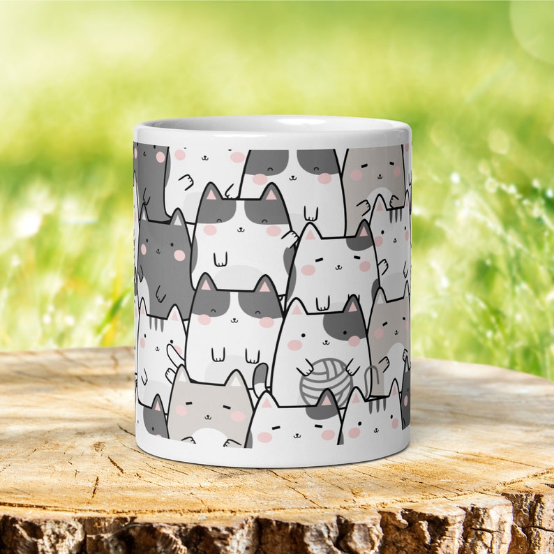 Pode incluir: Caneca de cer&acirc;mica branca com um padr&atilde;o repetitivo de gatos de desenho animado fofinhos em preto, branco e cinza. Os gatos est&atilde;o em v&aacute;rias poses, incluindo sentados, em p&eacute; e brincando com l&atilde;.