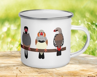Könnte beinhalten: Weiße Emailtasse mit einer bunten Illustration von drei Finken, die auf einem Ast sitzen. Die Vögel sind grau, braun und weiß mit roten Akzenten.