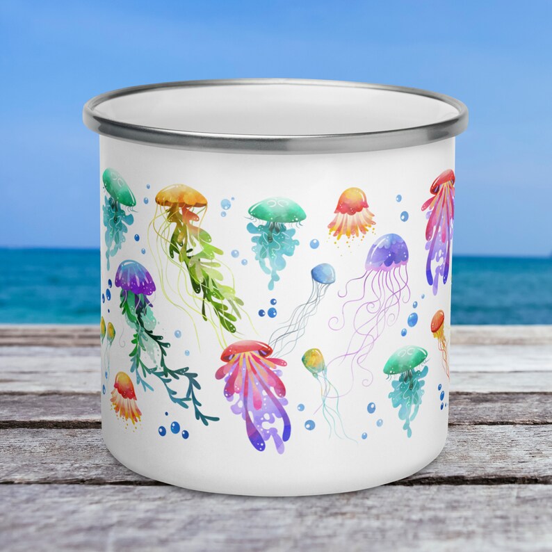 Pu&ograve; includere: Tazza smaltata bianca con un designo ad acquerello colorato di meduse. Le meduse sono di varie tonalit&agrave; di rosa, blu, verde, arancione e viola.