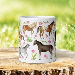May include: White ceramic mug with a colorful pattern of horses and pink flowers. The horses are brown, gray, and white with black manes and tails.