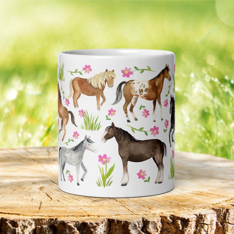 May include: White ceramic mug with a colorful pattern of horses and pink flowers. The horses are brown, gray, and white with black manes and tails.