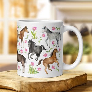 May include: White ceramic mug with a colorful watercolor design of horses and flowers. The horses are brown, black, gray, and brown and white. The flowers are pink.