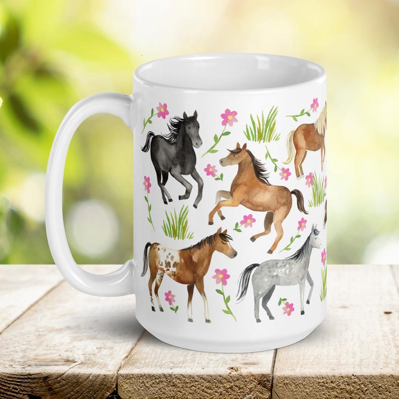 May include: White ceramic mug with a colorful design of horses and flowers. The horses are in various poses and colors, including brown, black, and white. The flowers are pink and green.