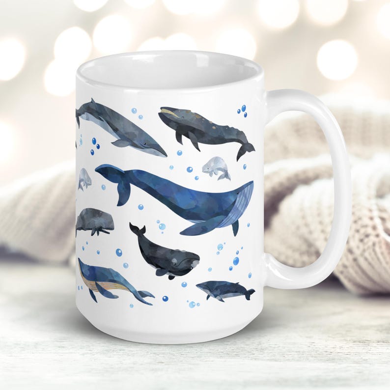 May include: White ceramic mug with a blue and gray watercolor design of various whale species. The whales are depicted swimming in a blue ocean with white bubbles.