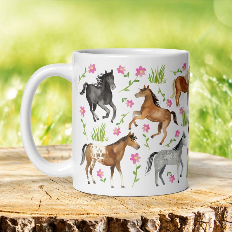 May include: White ceramic mug with a colorful design of horses and flowers. The horses are brown, black, and gray with pink flowers and green leaves.