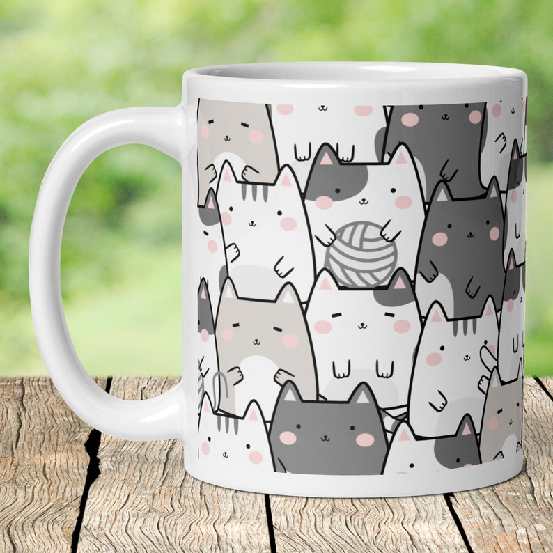 Pode incluir: Caneca de cer&acirc;mica branca com um padr&atilde;o de gatos de desenho animado em v&aacute;rios tons de cinza e branco. Os gatos s&atilde;o de diferentes tamanhos e t&ecirc;m express&otilde;es diferentes. Alguns dos gatos est&atilde;o segurando novelos de l&atilde;.