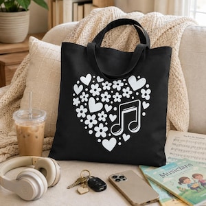May include: A black tote bag featuring a large white graphic design of a heart shape composed of various small flowers and hearts, with a prominent musical note symbol integrated into the right side of the heart pattern on the front panel.