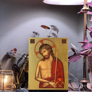 Può includere: Un'icona in legno che raffigura Gesù Cristo con una corona di spine, vestito con una tunica rossa e che tiene un bastone. L'icona ha uno sfondo dorato ed è incorniciata da una cornice in legno scuro. Il testo "ICON EXPERIENCE" è visibile nella parte inferiore dell'icona.