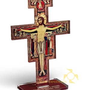 May include: A wooden crucifix with a detailed depiction of Jesus Christ, featuring red, gold, and brown tones. The cross has intricate artwork and stands on a rectangular base. The image includes religious figures and text.