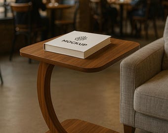 Può includere: Un tavolino in legno marrone con piano e base quadrati, collegati da una gamba curva. Un libro con la scritta "MOCKUP" è sul tavolo. Il tavolo si trova in un bar.