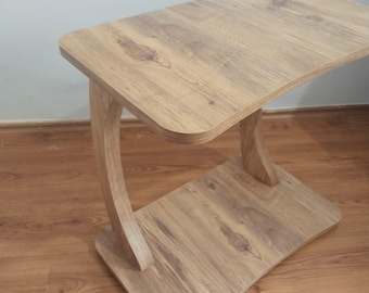 May include: A light brown wooden side table with a curved leg design. The table has a rectangular top and a lower shelf, both with a wood grain pattern. The table measures approximately 24 inches long, 12 inches wide, and 20 inches high.