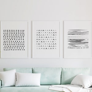 Pode incluir: Três impressões abstratas em preto e branco emolduradas em uma parede branca acima de um sofá verde claro com almofadas brancas.