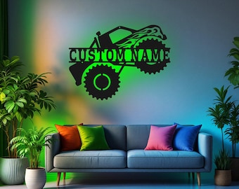 May include: Black metal silhouette of a monster truck with flames on the side and the words "CUSTOM NAME" above the wheels. The silhouette is mounted on a gray wall above a dark gray couch with colorful throw pillows.
