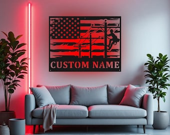 May include: Black metal wall art featuring an American flag design with a lineman working on a power line. The flag's stars are visible, and the text "CUSTOM NAME" is below. The art is illuminated with red light.
