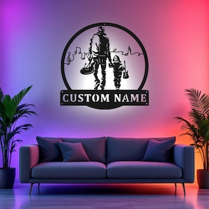 May include: Black metal wall art depicting a parent and child walking together, each holding a guitar. The design is set within a circular frame with musical notes and the text "CUSTOM NAME" below. The background features a gradient of purple, pink, and orange.