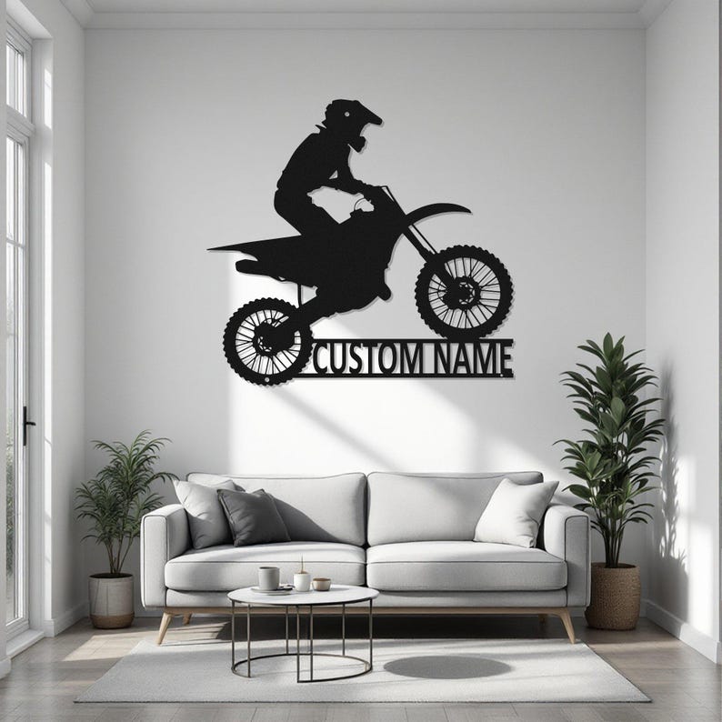 May include: Black metal silhouette of a motocross rider jumping a dirt bike. The silhouette is mounted on a white wall above a gray couch. The text "CUSTOM NAME" is below the silhouette.