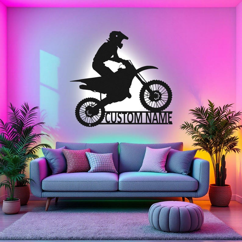 May include: A black silhouette of a motocross rider jumping a dirt bike with the text "CUSTOM NAME" below. The image is set against a pink and purple gradient background with a couch and a plant in the foreground.