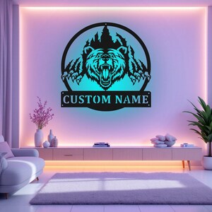 May include: A black metal wall decor featuring a bear head emerging from a mountain silhouette. The bear has a fierce expression and is outlined in a blue glow. The text "CUSTOM NAME" is displayed below the bear.