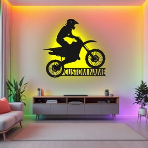 May include: Black silhouette of a motocross rider on a dirt bike with the text "CUSTOM NAME" below. The image is on a wall with colorful LED lights.