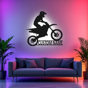 May include: A black silhouette of a motocross rider on a dirt bike with the text "CUSTOM NAME" below. The image is set against a wall with colorful lighting.