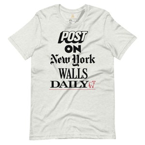 Może przedstawiać: Biała koszulka z czarnym napisem "POST ON NEW YORK WALLS DAILY" i małym czerwonym wizerunkiem byka.