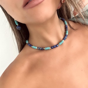 May include: A gold chain necklace with blue and turquoise beads. The necklace is layered with small gold beads.