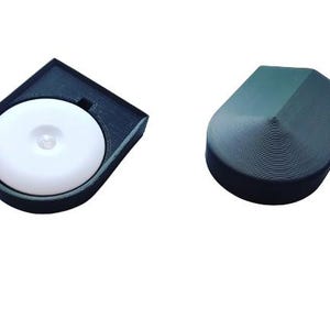 Peut inclure: Deux lampes à détecteur de mouvement en plastique noir. Une lampe a une surface d'émission de lumière ronde et blanche. L'autre lampe a un sommet arrondi et pointu.