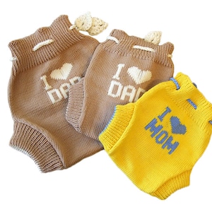 May include: Three knitted baby bloomers with different colors and designs. One pair is brown with "I love Dad" in white lettering. Another pair is brown with "I love Dad" in white lettering. The third pair is yellow with "I love Mom" in blue lettering.