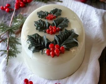 May include: A white round cake decorated with green holly leaves and red berries. The cake is on a white cloth.
