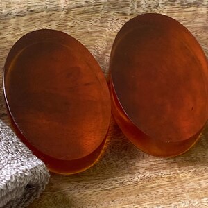 May include: Two oval-shaped amber-colored soap bars on a wooden surface.