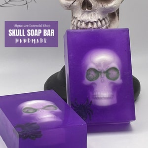 May include: Two purple soap bars with a white skull design and a black spider. The soap bars are handmade and have the text "Skull Soap Bar Handmade" on the front.