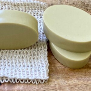 May include: Three oval-shaped bars of green soap on a wooden surface. One bar is on a white mesh soap saver.