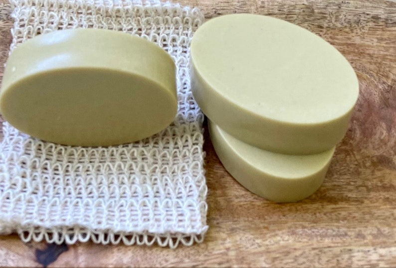 May include: Three oval-shaped bars of green soap on a wooden surface. One bar is on a white mesh soap saver.