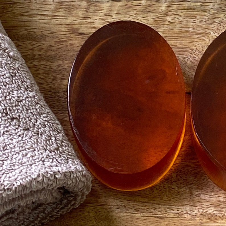 May include: Two round, amber-colored soap bars on a wooden surface. The soap bars are smooth and shiny.